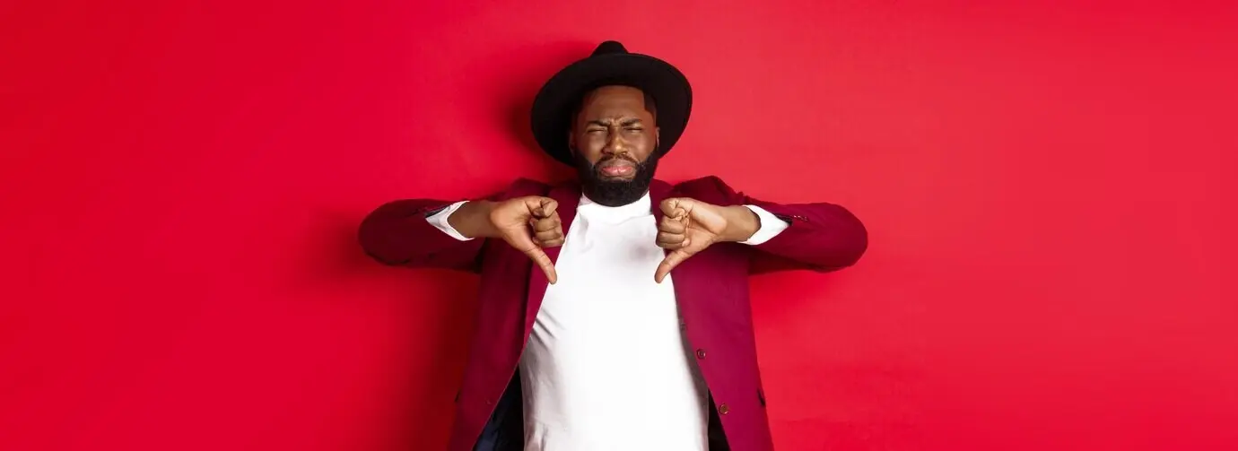 Разочарованный чернокожий мужчина оставляет негативный отзыв, показывая палец вниз и морщась от неприязни.